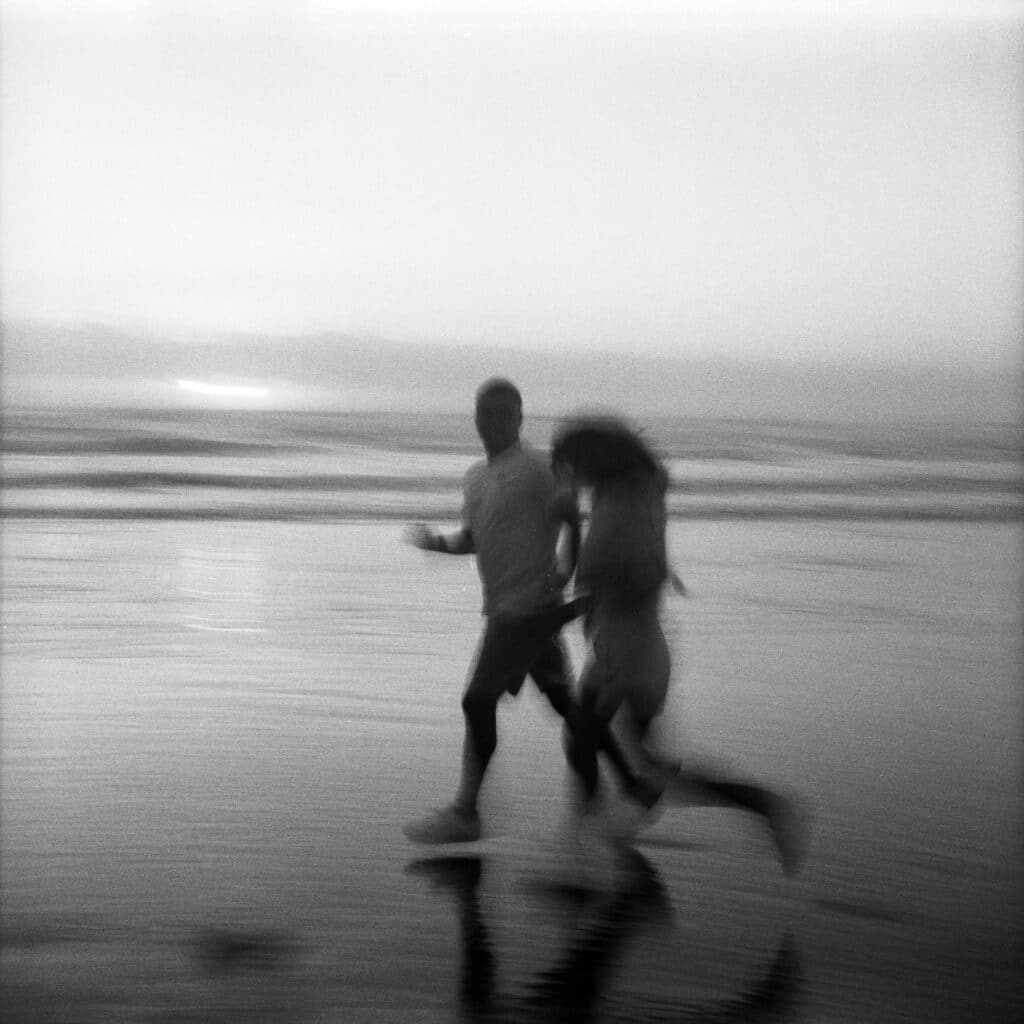 black and white film photo of couple running on beach at sunset during oregon coast elopement