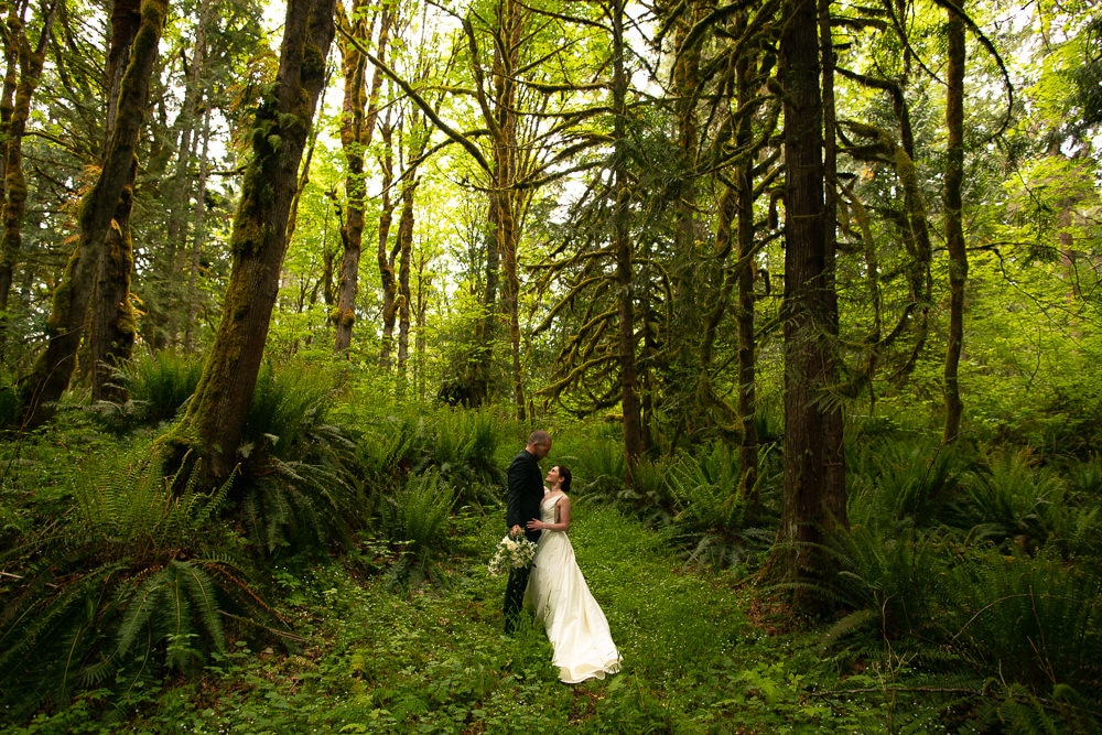 Couple looks at each other in green forest during washington state elopement