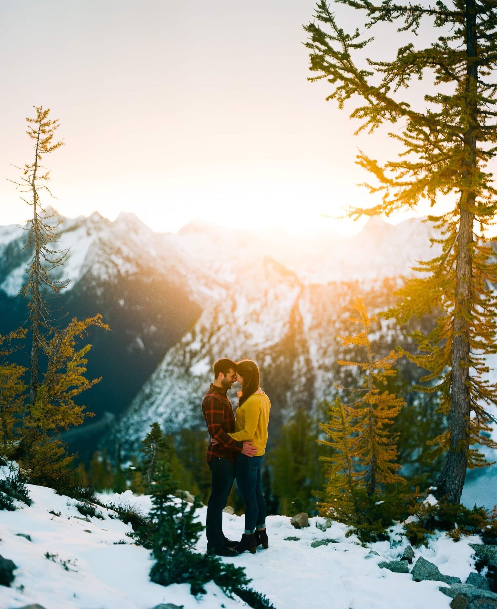 couple stands together on and looks out on sunset cascade mountains engagement