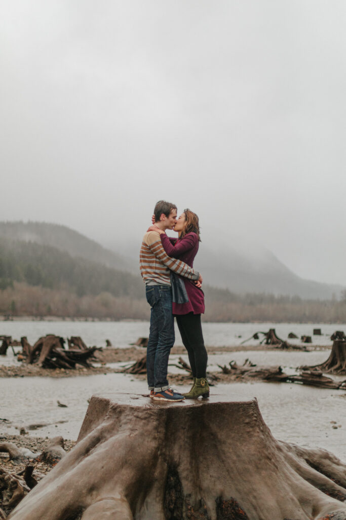 couple kisses standing on stump during winter proposal