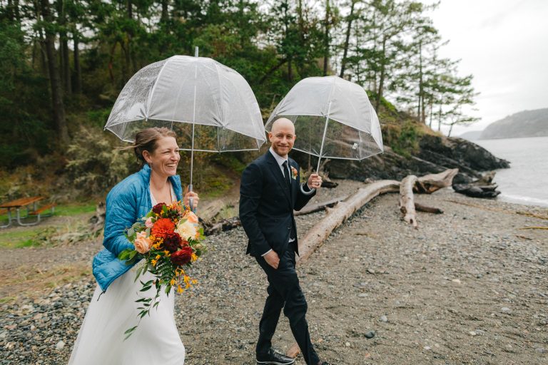 couple smiles with umbrellas during rainy elopement