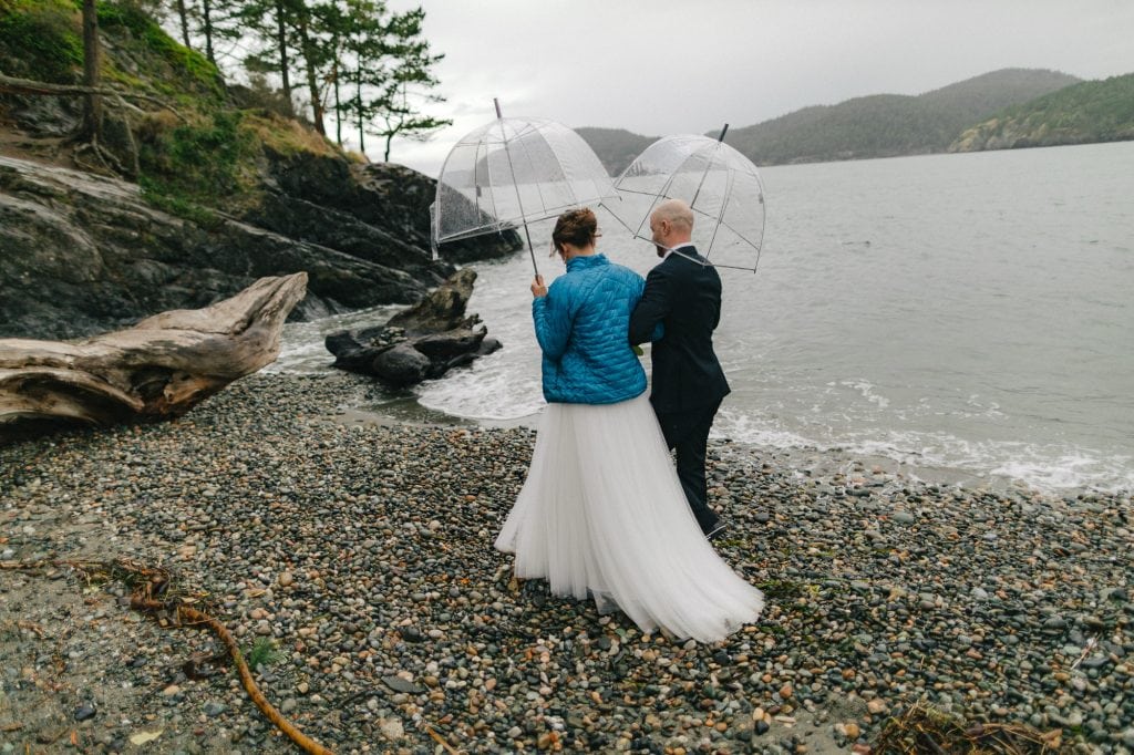 couple walks on beach with umbrellas Deception Pass State Park elopement